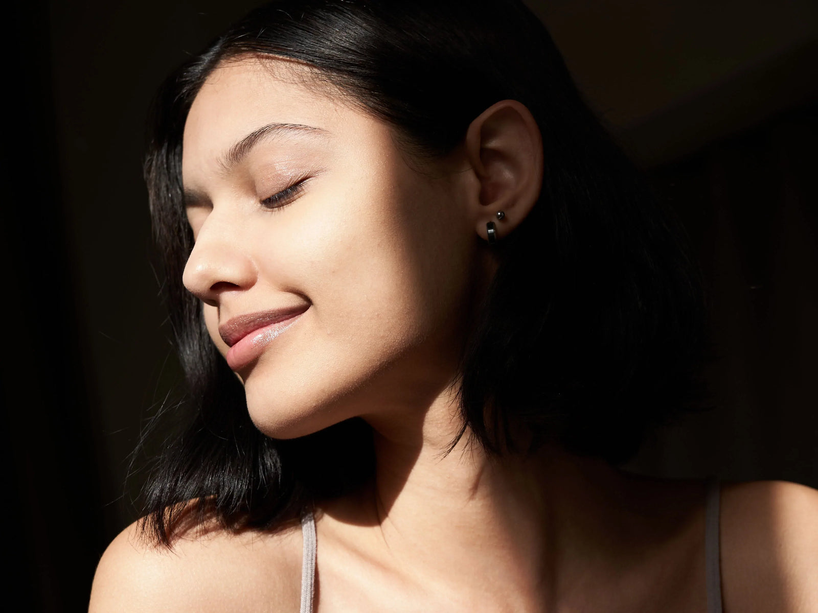 woman smiling after a chemical peel looking at her clear skin on a dark background