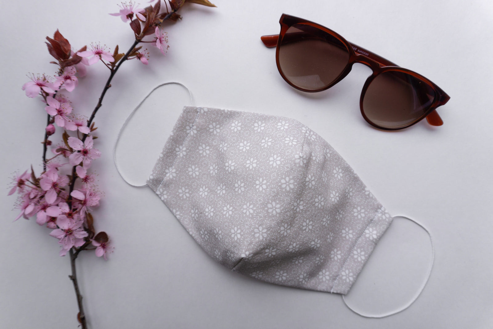 face mask on a grey background with a plant and sunglasses